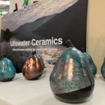 A large copper-green pear sits in front of Ullswater Ceramics sign