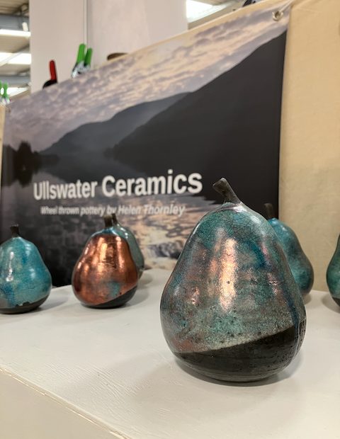 A large copper-green pear sits in front of Ullswater Ceramics sign